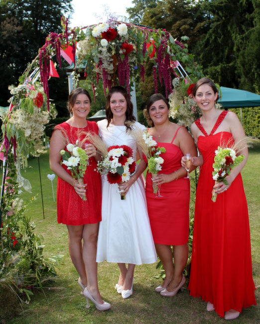 Bridesmaids in red dresses beneath a floral arch