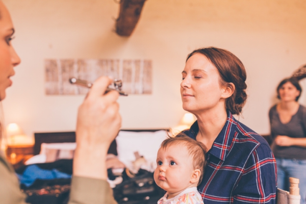Bride having make-up done with baby on her lap // Cosy winter wedding at River Cottage // Larissa Joice Photography // The Natural Wedding Company